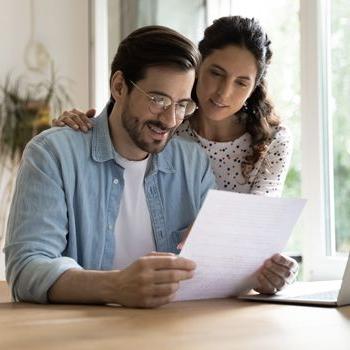 A mom and dad review a bank statement at a dining table.